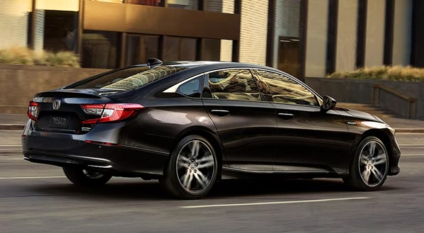 A black 2021 Honda Accord Hybrid is driving through a city after leaving a Honda Accord dealer.