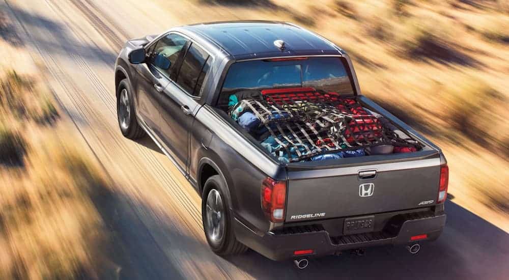 A grey 2021 Honda Ridgeline is driving down a dirt road with a bed full of camping gear.