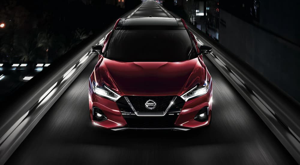 A red 2021 Nissan Maxima is driving through a city at night.