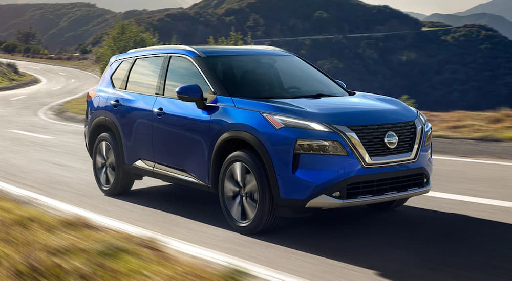 A blue 2021 Nissan Rogue is driving down an open road.