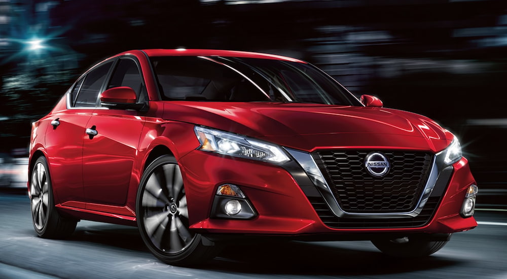 A red 2021 Nissan Altima is driving through a city at night after leaving a car dealer.