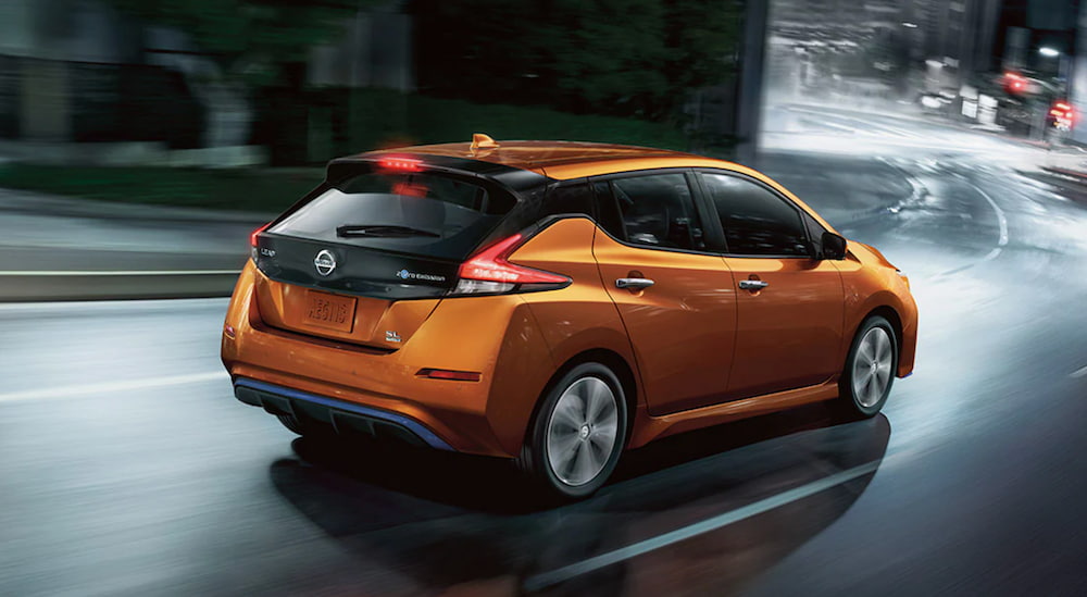 A orange 2021 Nissan Leaf is shown from an angle driving through a city at night.