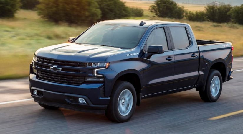 A dark blue 2019 Chevy Silverado is driving on an open road after leaving a used Chevy Silverado dealer.