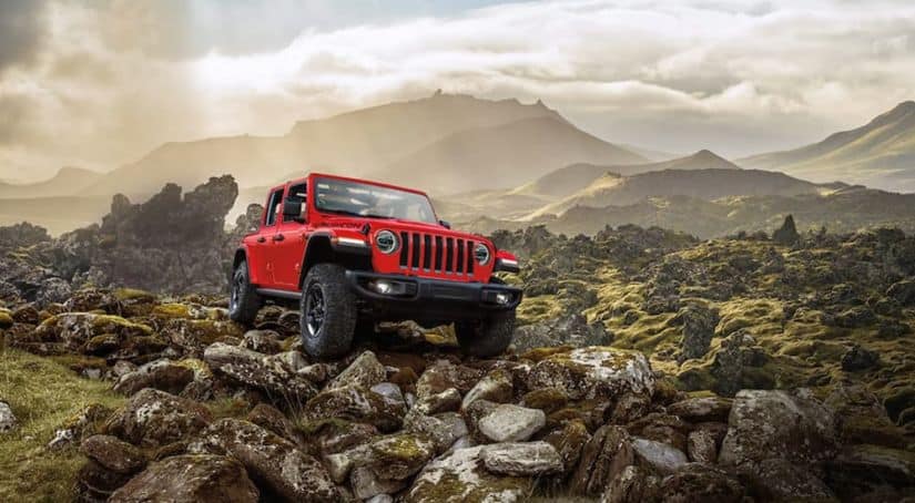 A red 2021 Jeep Wrangler Unlimited Rubicon is shown driving over rocks after leaving a used Jeep dealership.