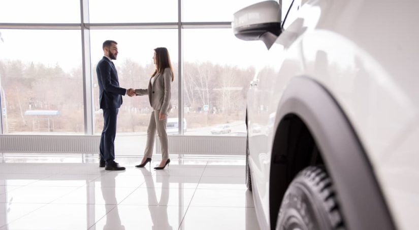 A man and woman are shaking hands in a salesroom at used car dealership.