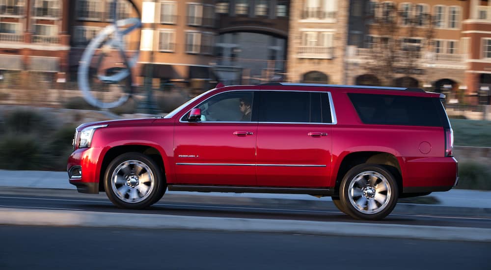 A red 2017 GMC Yukon XL Denali is shown from the side as it drives past a city.