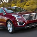 A popular used family car for sale, a red 2019 Cadillac XT5 Platinum, is driving down a tree-lined road.