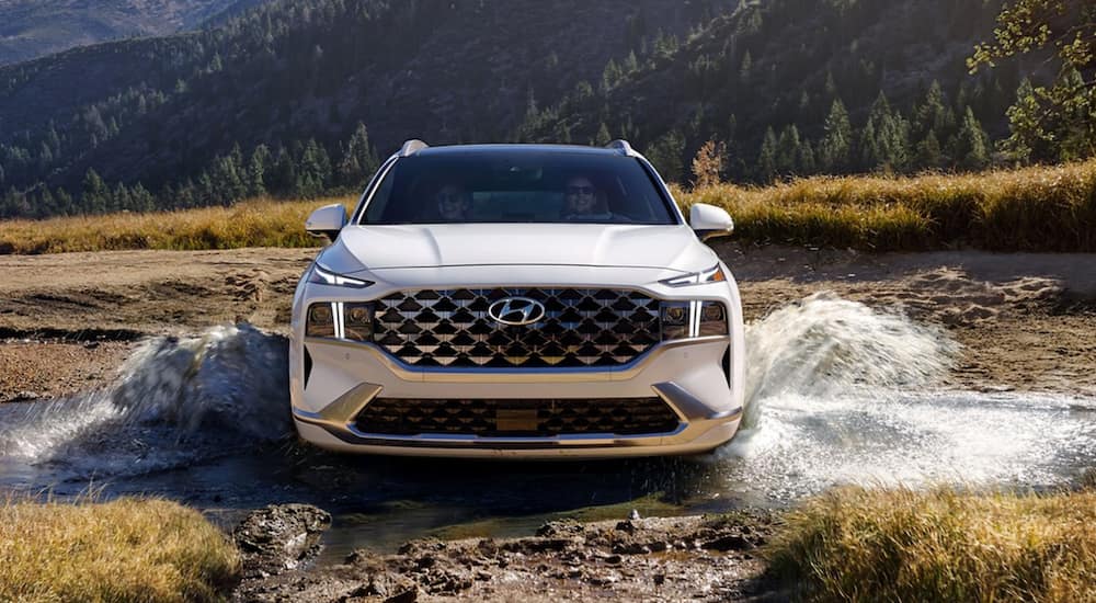 A white 2021 Hyundai Santa Fe is off-roading through a mud puddle in an open field.