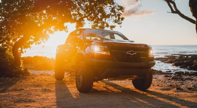 A red 2021 Chevy Colorado ZR2 is shown parked on the beach at sunset.