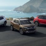 A white, a red, and a brown 2021 Chevy Trailblazer are parked on pavement in front of the ocean.