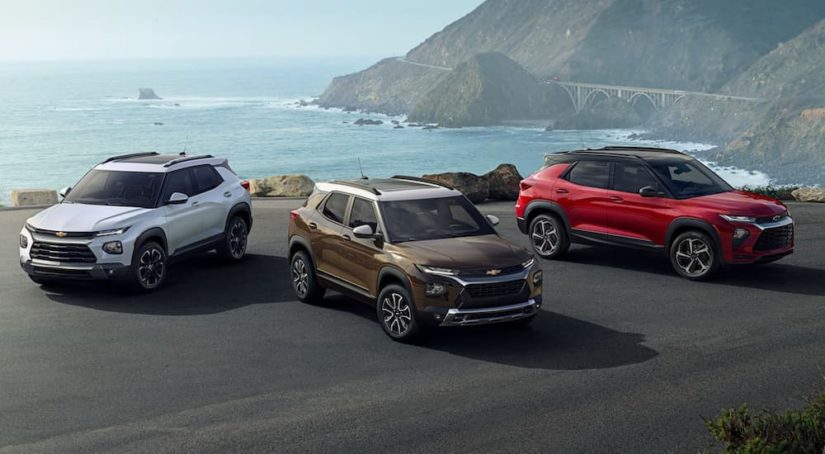 A white, a red, and a brown 2021 Chevy Trailblazer are parked on pavement in front of the ocean.