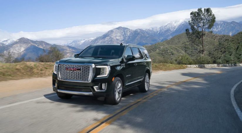 A black 2021 GMC Yukon is shown driving on a two way road overlooking mountains.
