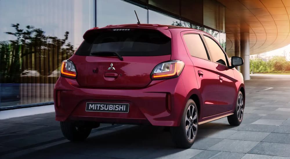 A red 2021 Mitsubishi Mirage is shown from the back parked in front of a modern building.