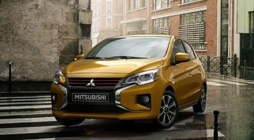 A yellow 2021 Mitsubishi Mirage is shown turning on a city street in the rain.
