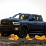 A blue 2021 Ram 2500 is shown from the side parked in a grass field at sunset.