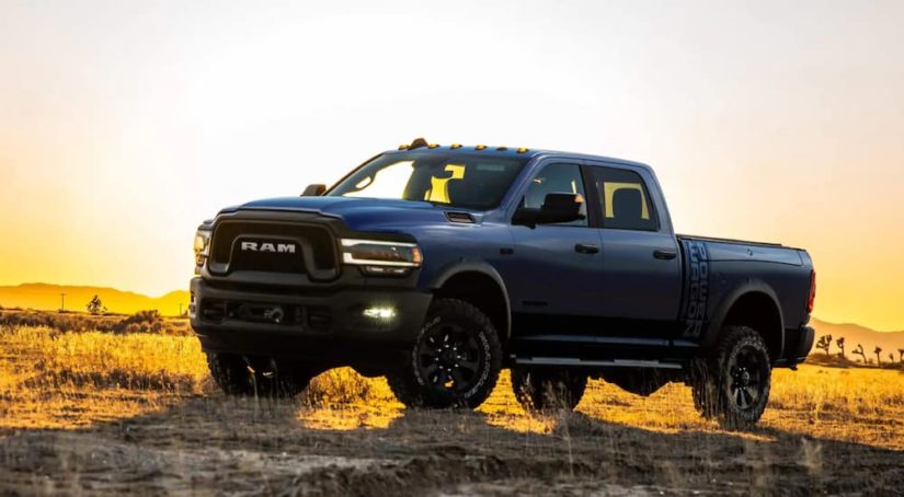 A blue 2021 Ram 2500 is shown from the side parked in a grass field at sunset.