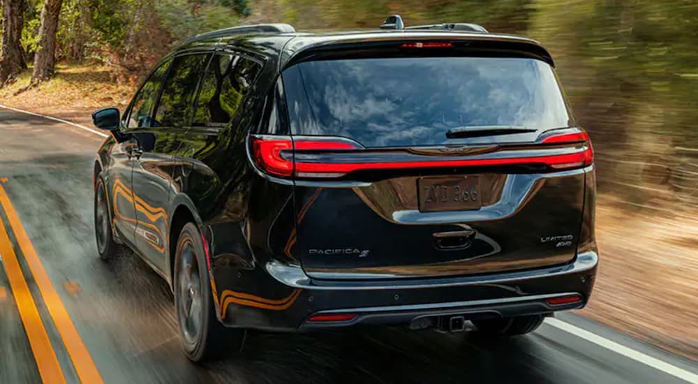 A black 2021 Pacifica is shown from the back driving on a tree lined road.