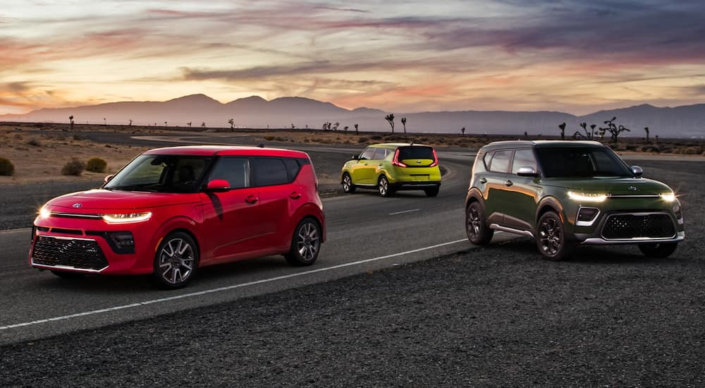 An orange, a green, and a yellow 2021 Kia Soul are parked on pavement at sunset.