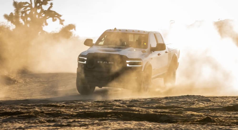 A white 2021 Ram 2500 is driving through a dusty desert in low lighting.