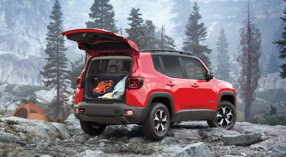 A red 2021 Jeep Renegade is parked on snow dusted rocks in the mountains.