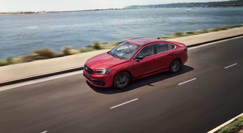 A red 2021 Subaru Legacy is driving next to the ocean after leaving a Subaru Legacy dealer.