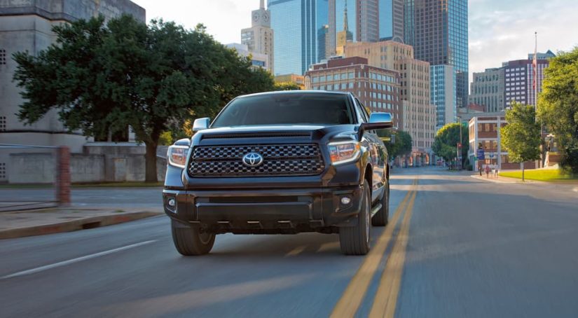 A popular current model used truck is shown, a black 2021 Toyota Tundra Platinum CrewMax, is driving down a city street.