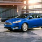 A blue 2018 Ford Focus is parked inside a used Ford Focus dealer in front of a woman.