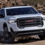 A 2020 GMC Acadia is shown from the front off-roading in the mountains after leaving a used GMC SUV dealer.