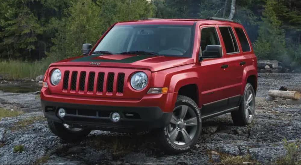 A used red 2020 Jeep Patriot is parked on crushed stone in front of a forest.