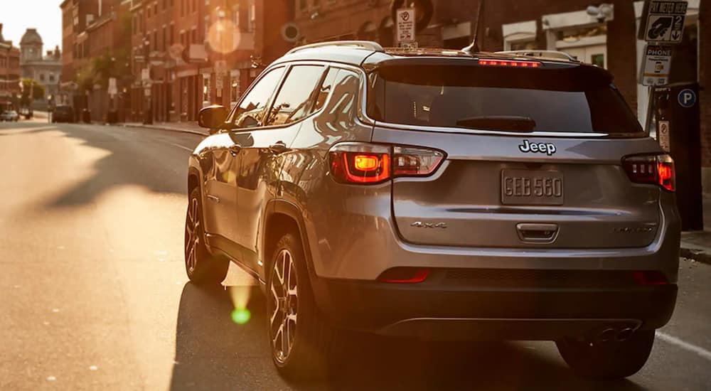 A used silver 2020 Jeep Compass is driving through a city at sunset.