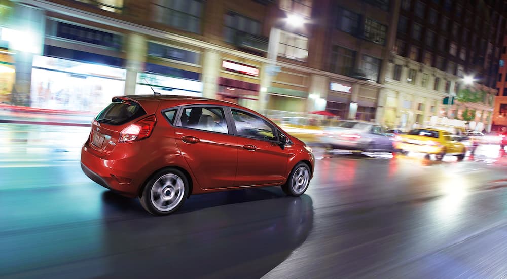 A red 2018 Ford Fiesta is driving through a city after looking at used cars for sale.