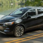 A black 2021 Buick Encore is driving on a two way road past a lake during a 2021 Buick Encore vs 2021 Buick Encore GX comparison.