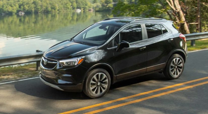 A black 2021 Buick Encore is driving on a two way road past a lake during a 2021 Buick Encore vs 2021 Buick Encore GX comparison.