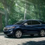 A blue 2021 Chevy Equinox is parked outside of a modern home in the forest.