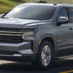 A grey 2021 Chevy Tahoe is shown from the side driving down an open road.