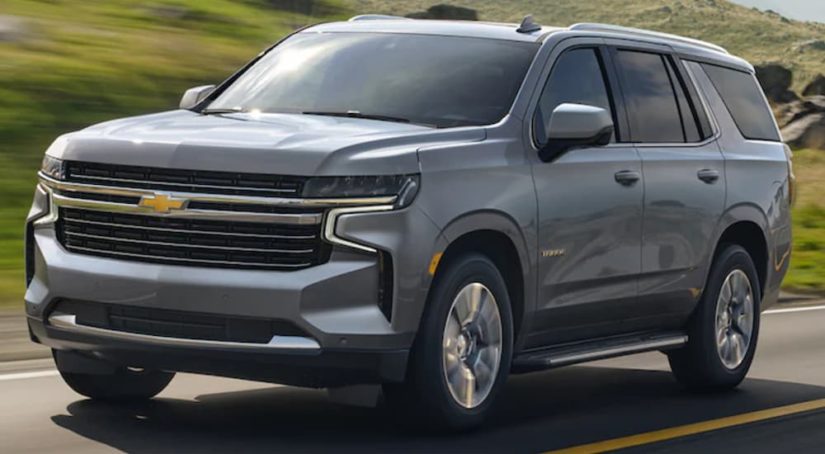 A grey 2021 Chevy Tahoe is shown from the side driving down an open road.