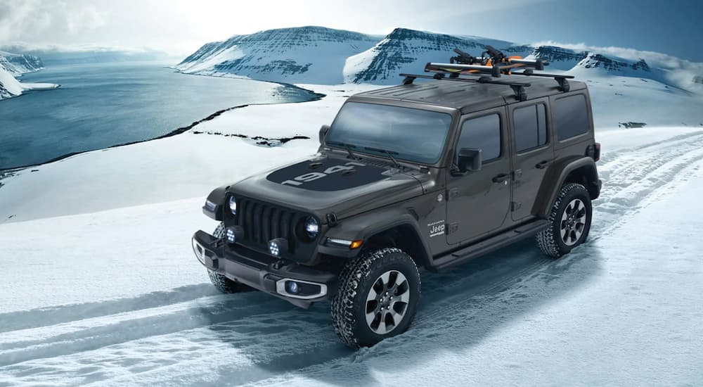 A grey 2021 Jeep Wrangler 1941 edition is shown driving on a snow covered road. 
