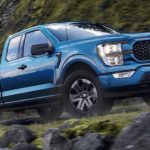 A blue 2021 Ford F-150 is driving on a mountain after winning a 2021 Ford F-150 vs 2021 Ram 1500 comparison.