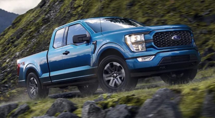 A blue 2021 Ford F-150 is driving on a mountain after winning a 2021 Ford F-150 vs 2021 Ram 1500 comparison.