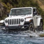 A white 2021 Jeep Wrangler Rubicon is shown driving through water after winning the 2021 Jeep Wrangler vs 2021 Ford Bronco shoot-out.