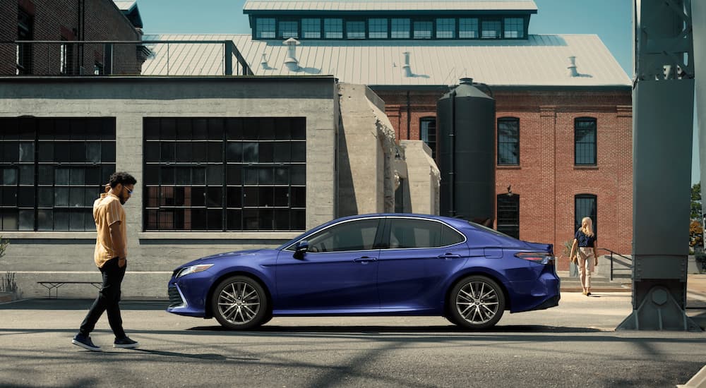 A blue 2021 Toyota Camry is shown from the side parked in a city.