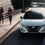 A white 2021 Nissan Sentra is shown from the front driving through a city.