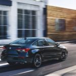 A black 2022 Honda Civic Sport is shown from the back driving through a city during a 2022 Honda Civic vs 2021 Honda Civic comparison.