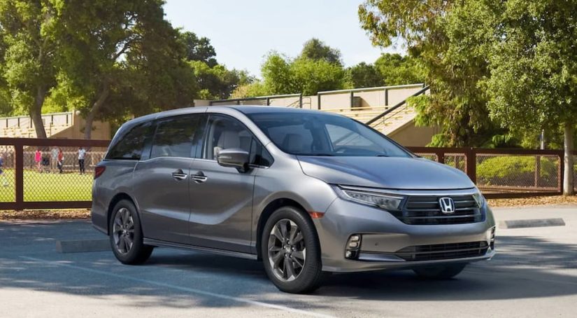 A grey 2022 Honda Odyssey Elite is parked in front of a soccer field after winning a 2022 Honda Odyssey vs 2021 Chrysler Pacifica comparison.