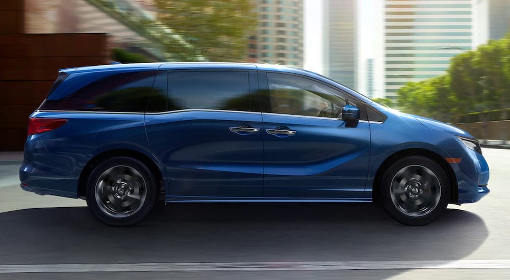 A blue 2022 Honda Odyssey Elite is driving through a city.