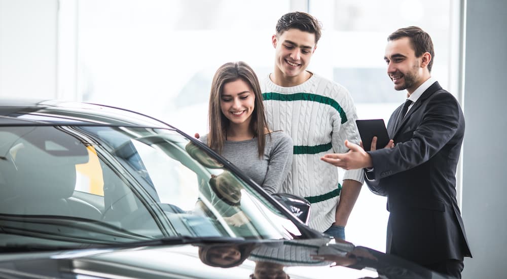 A salesman is shown with a couple looking at a car.
