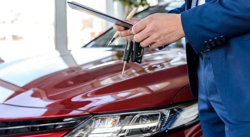 A close up shows a salesman with car keys next to a red sedan.