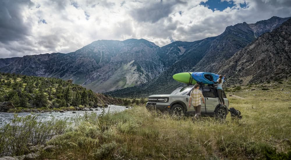 A tan 2021 Ford Bronco Sport is parked next to a river with two kayaks on top.