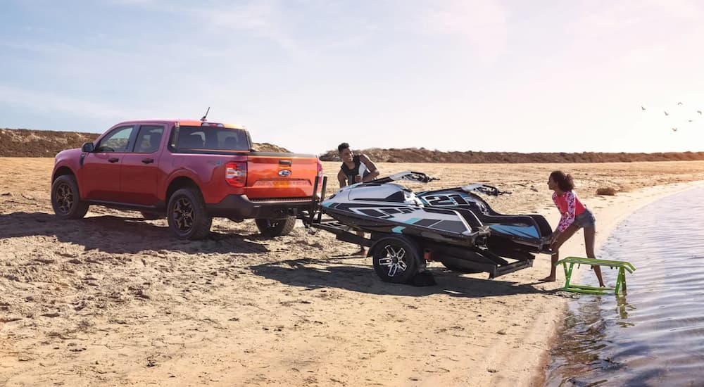 An orange 2022 Ford Maverick is being used to tow a jet-ski on the beach.