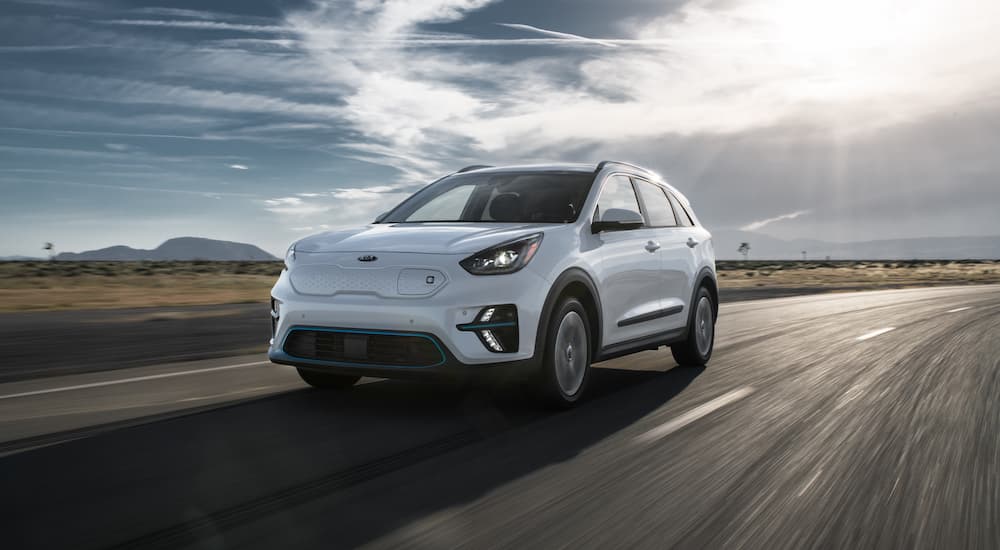 A white 2020 Kia Niro EV is driving on a road on a cloudy day.